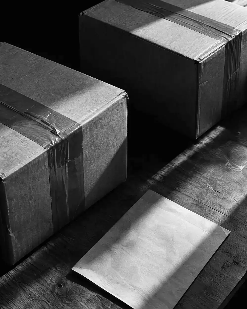 Paket mit Klebeband und Lieferschein auf einem Holztisch, daneben ein zweites Paket im Seitenlicht