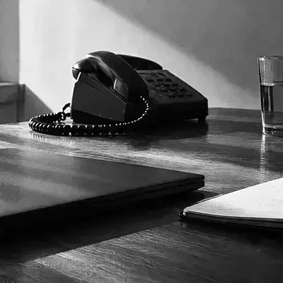 Schreibtischtelefon und ein Glas Wasser auf einem Holztisch, daneben eine Mappe