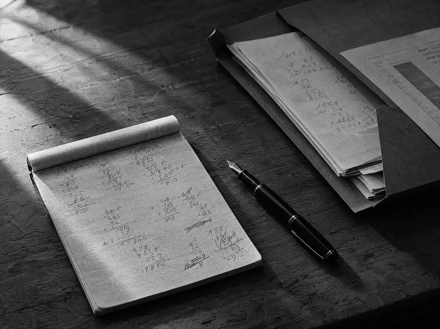 Notizblock mit handschriftlichen Zahlen und Füllfederhalter, daneben ein offener Ordner mit Unterlagen auf einem Holztisch