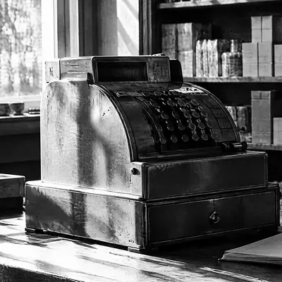 Ladentheke mit Kasse und aufgeschlagenem Notizblock, dahinter Regale voller Waren