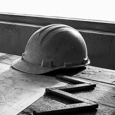 Bauplan-Rolle und ausgebreiteter Bauplan mit unleserlichen Linien, Zollstock und Bauhelm auf rohem Holz, hartes Seitenlicht