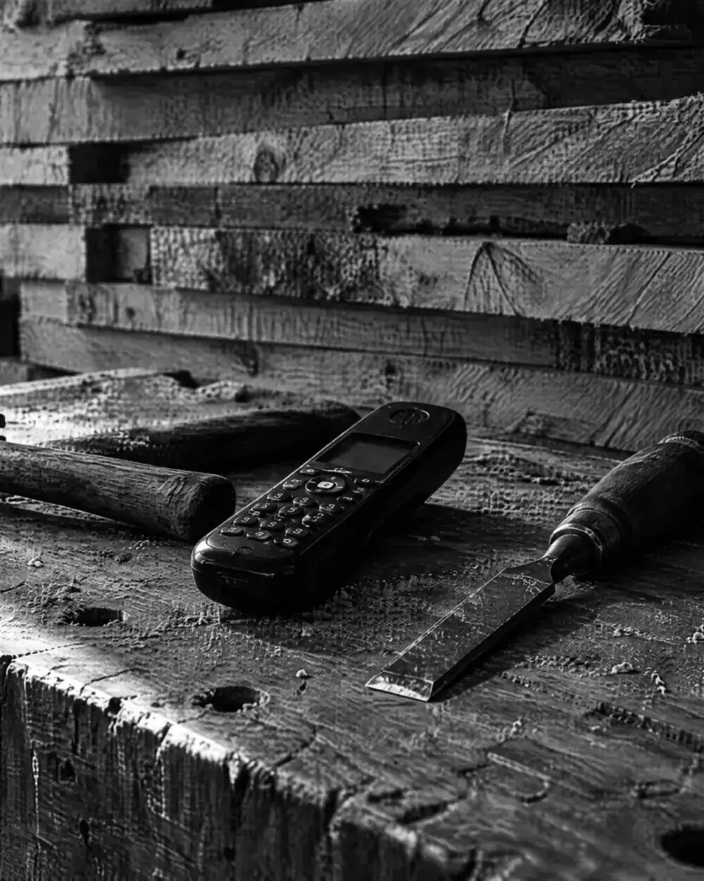 Schnurloses Telefon zwischen Hammer und Stechbeitel auf einer Werkbank