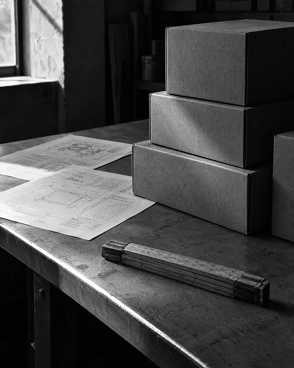 Gestapelte Produktkartons mit unleserlichen Datenblättern und einem zusammengeklappten Zollstock auf einem Tisch